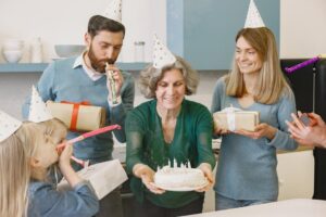 A happy family celebrating with gifts, cake, and party hats indoors, showcasing togetherness and joy.