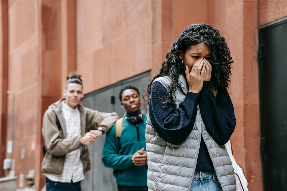 From below of despaired young ethnic female student covering mouth with hands while crying on street after being bullied by m