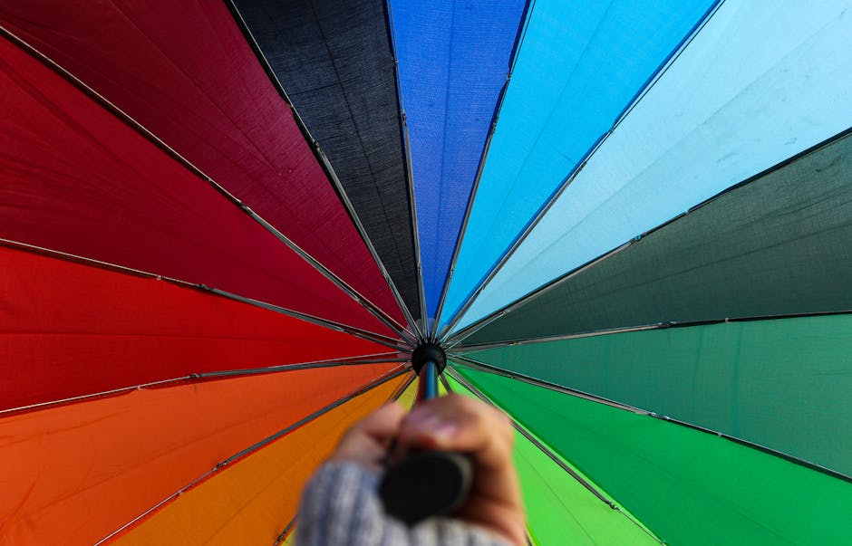 Vibrant rainbow umbrella viewed from below, capturing its vivid colors against daylight.