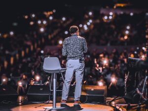 Speaker addressing large audience with phones lit up at night event.