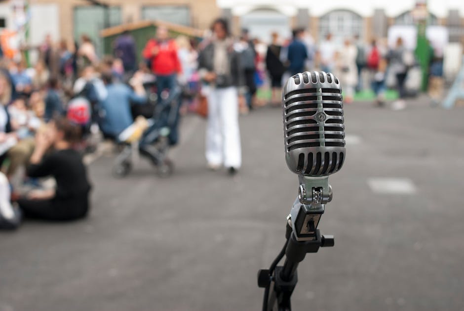 Close-up of a vintage microphone with blurred crowd in the background, capturing a lively outdoor event.