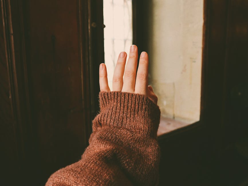 A hand wearing a wool sweater reaching towards a window, featuring warm tones and soft textures.