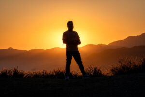 A silhouette of a person on Mount Baldy at sunset, capturing the vibrant orange sky.