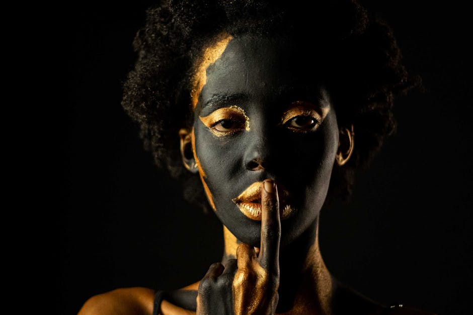 Striking portrait of an African woman with artistic makeup in gold and black set against a dark background.