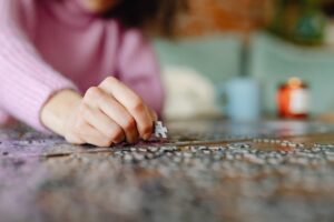 A person in a pink sweater assembling a jigsaw puzzle on a table with blurred background.