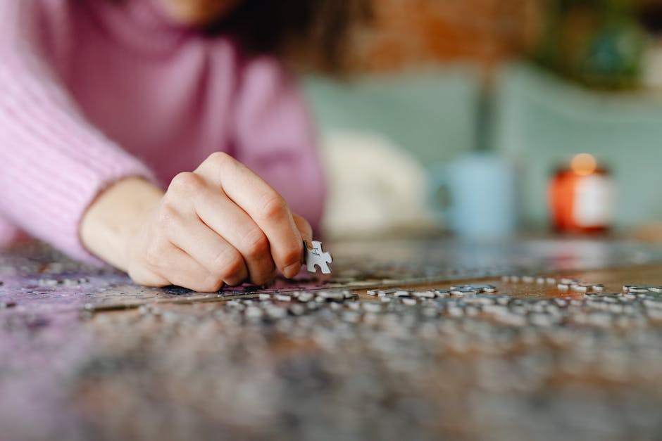 A person in a pink sweater assembling a jigsaw puzzle on a table with blurred background.