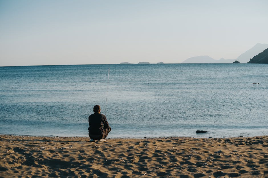 A solitary figure sits by the seaside fishing at dawn, exuding calm and tranquility.