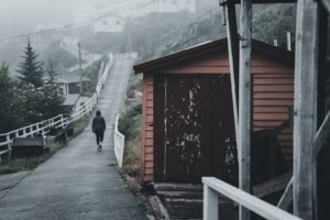 A lone figure walks down a foggy urban alley beside a rustic orange shed.