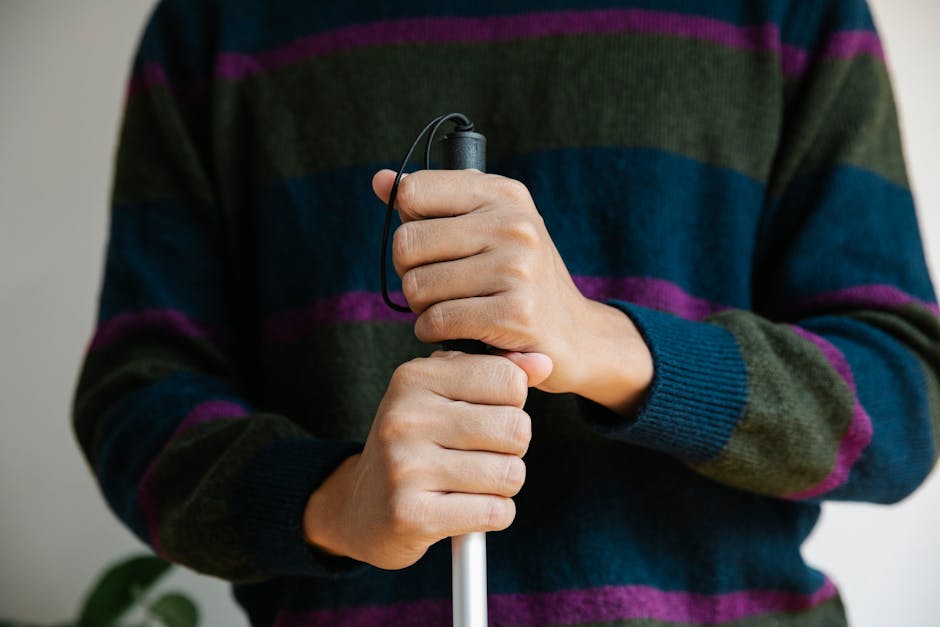 Close-up of hands gripping a walking stick, wearing a striped sweater indoors.