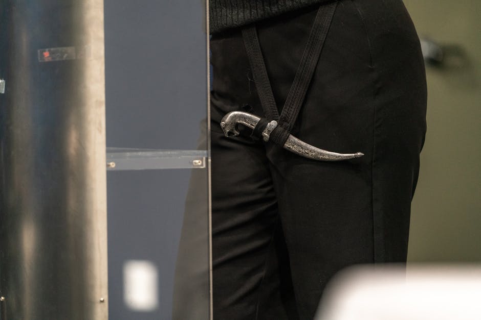 A close-up shot of an intricately designed dagger secured in a belt loop on black pants indoors.