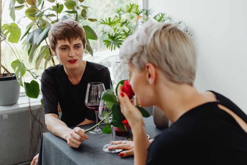 Two women enjoying a romantic indoor date with wine and roses amidst lush greenery.