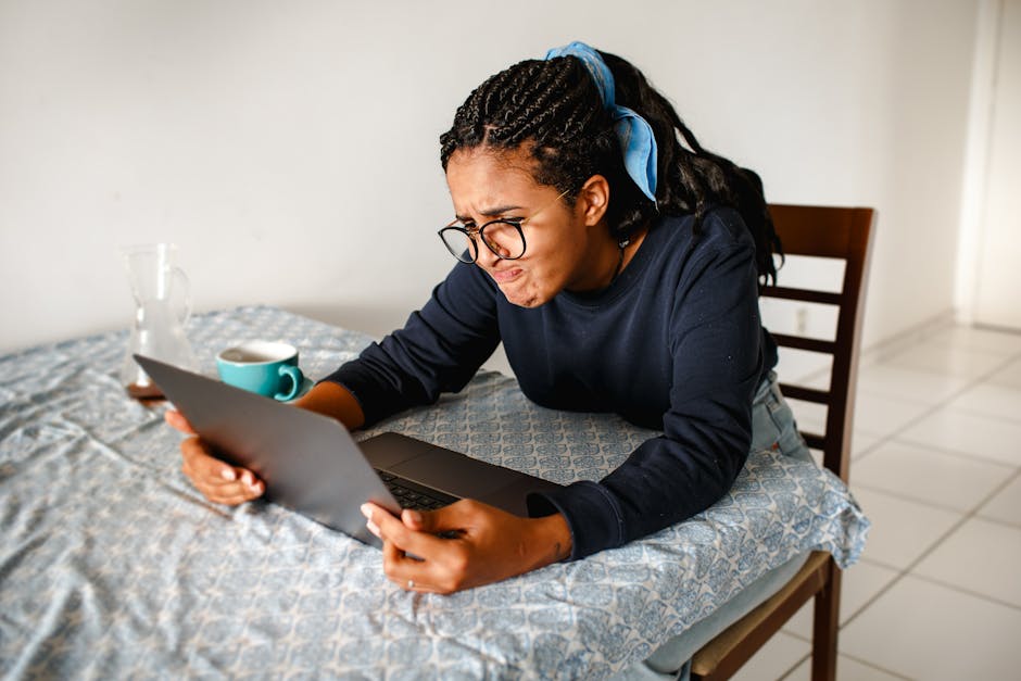 A young woman expressing frustration while using a laptop at home.