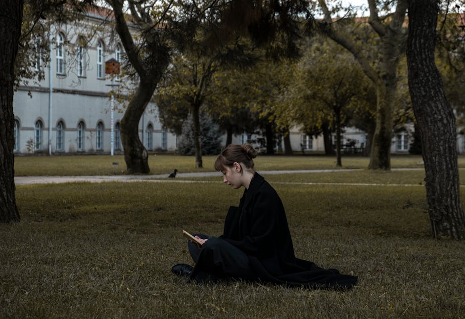 Young woman in a black coat reading in a peaceful park environment.