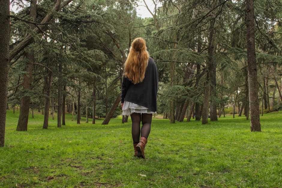 A girl with long hair walks through a lush green park in Madrid, surrounded by trees.